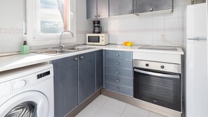 A compact kitchen with grey cabinets, a microwave, a sink, a washing machine, and a stove. - Aiguablava Apartments 3 (Begur)