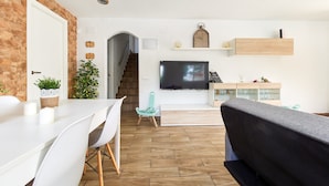 A modern living room with a TV, white furniture, a staircase, and a wooden floor.