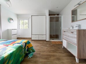 Une chambre à coucher comprenant un lit, une armoire, un dressing, une salle de bain avec douche et un miroir.