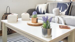 A white table with decorative items, a grey sofa with patterned cushions, and a window with natural light.