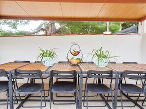 Un patio al aire libre con una mesa de madera y sillas negras, rodeado de plantas en macetas.