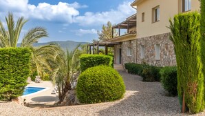 A house with a swimming pool, surrounded by well-maintained hedges and palm trees.