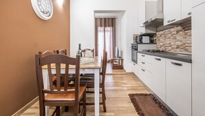 Une cuisine de taille réduite avec des meubles blancs, une table à manger en bois et une horloge au mur.