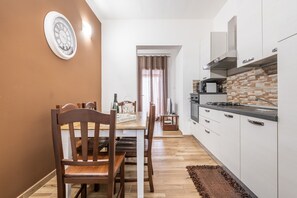 Une cuisine de taille réduite avec des meubles blancs, une table à manger en bois et une horloge au mur.