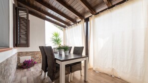 Une terrasse couverte avec une table et des chaises, une plante en pot et une vue sur l’extérieur.