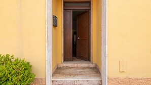 Un escalier mène à une porte en bois, et un petit coffret aux lettres est fixé au mur, sur le côté gauche.