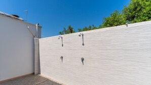 Una terraza con un muro blanco de azulejos, tres salidas de agua y un rincón con un muro blanco y una tubería.