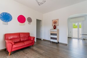 A spacious room with a red leather sofa, wooden flooring, a white cabinet, and wall decorations.