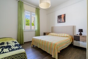 Une chambre à coucher avec un lit, une table de chevet, une lampe, une fenêtre avec des rideaux et un tableau au mur.