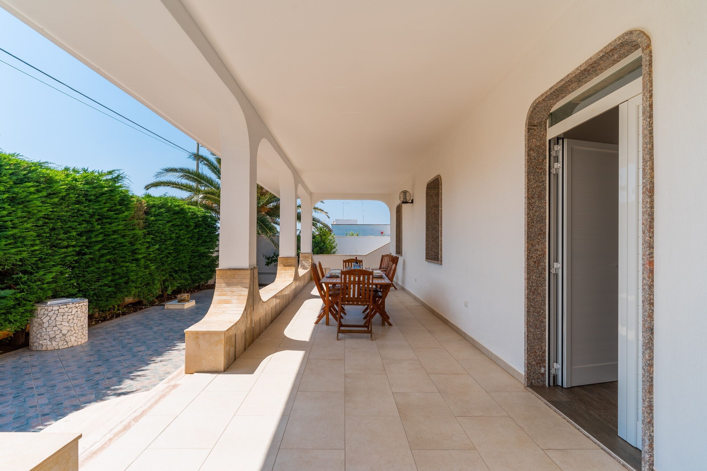 A covered outdoor area with a table and chairs, a stone planter, and a door leading to a room.