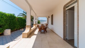 Un espacio al aire libre techado con una mesa, sillas, una jardinera de piedra y una puerta que da a una habitación.