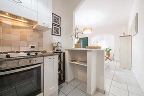 A compact kitchen with a gas stove, oven, white cabinets, and a small island with a sink.