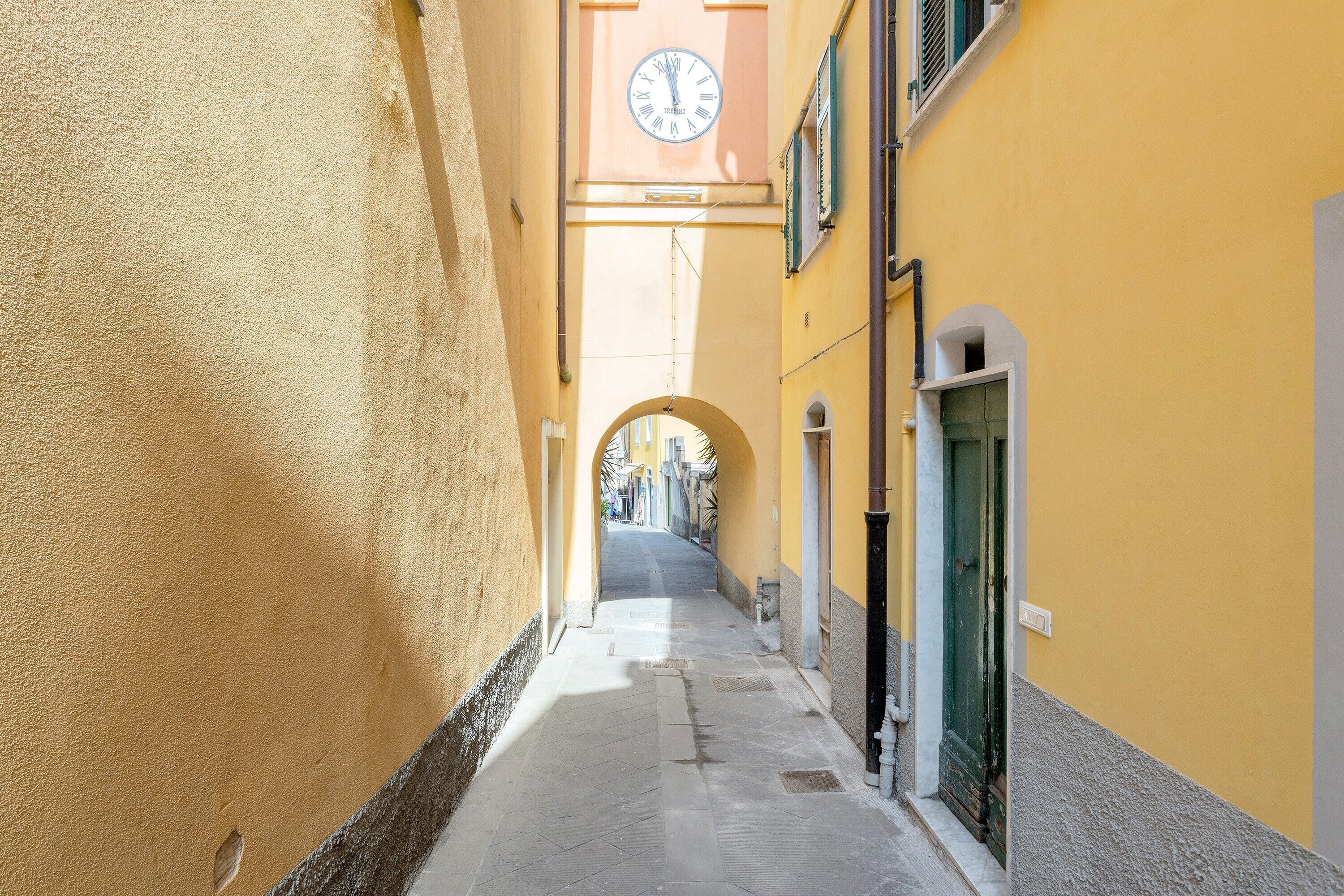Une ruelle étroite bordée d’immeubles jaunes, avec une tour de l’horloge et un arc de triomphe.