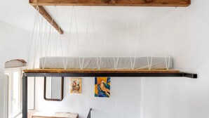 Een kamer met een houten balkenplafond, een hangend net en twee schilderijen aan de muur.
