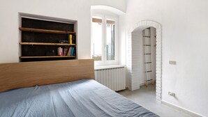 Een slaapkamer met een bed, een boekenkast, een raam en een witte bakstenen muur.