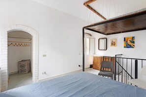 Ein Schlafzimmer mit einem Bett, einem Holzstuhl, einem kleinen Tisch, einem Kleiderständer und einer Wäschetasche.
