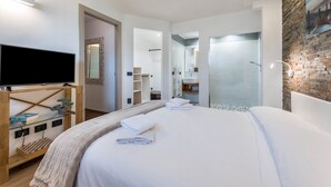 A modern hotel room with a large bed, a flat-screen TV, a wooden side table with a plant, and a stone accent wall. - Apartment 'Georesort D2' with Mountain View, Wi-Fi and Air Conditioning (Tremosine)