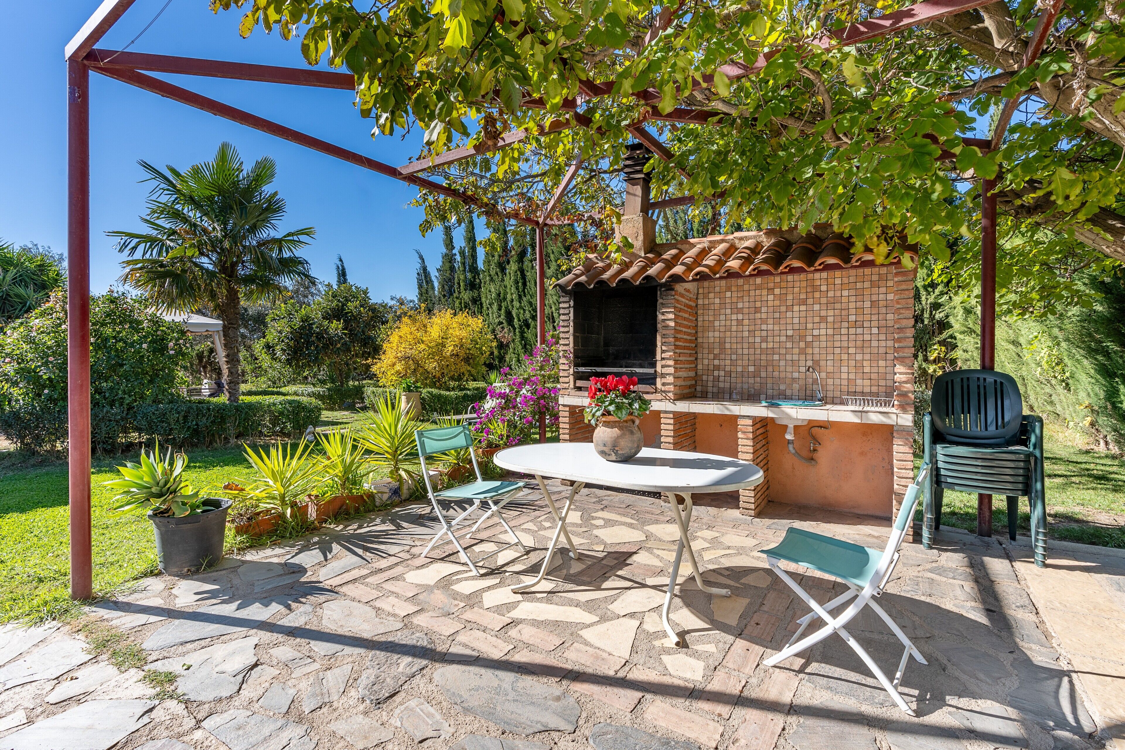 Une terrasse extérieure avec un barbecue en briques, une table, deux chaises et une pergola.
