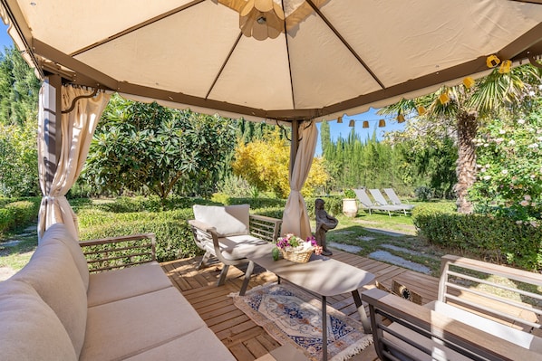 A covered outdoor seating area with a sofa, a table, and a bench.