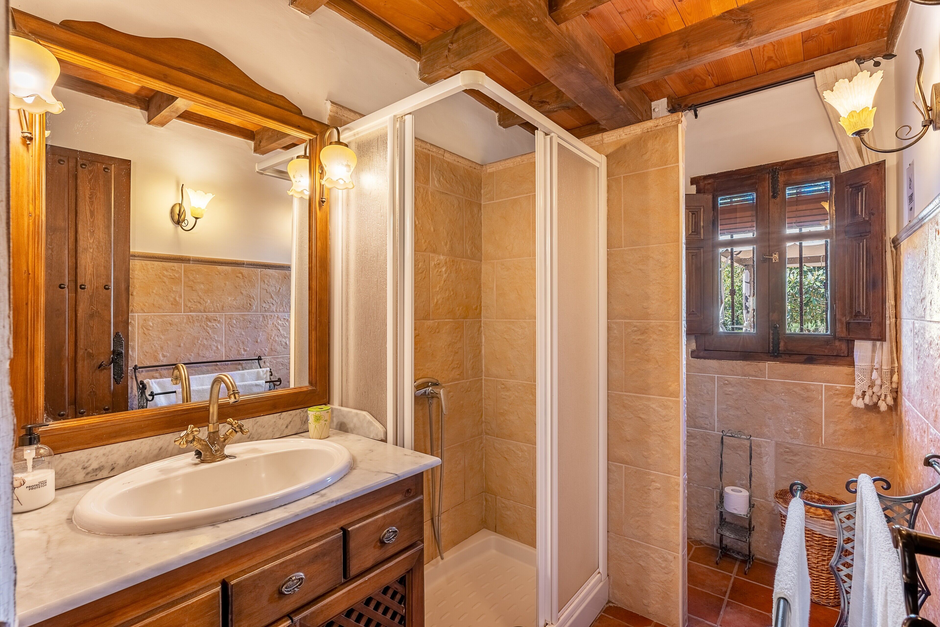 A bathroom with a sink, mirror, shower, wooden beams, and a window.