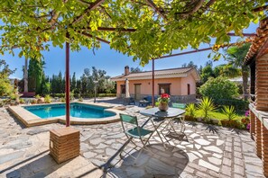 A pool area with a pergola, a brick house, and a patio with a table and chairs.
