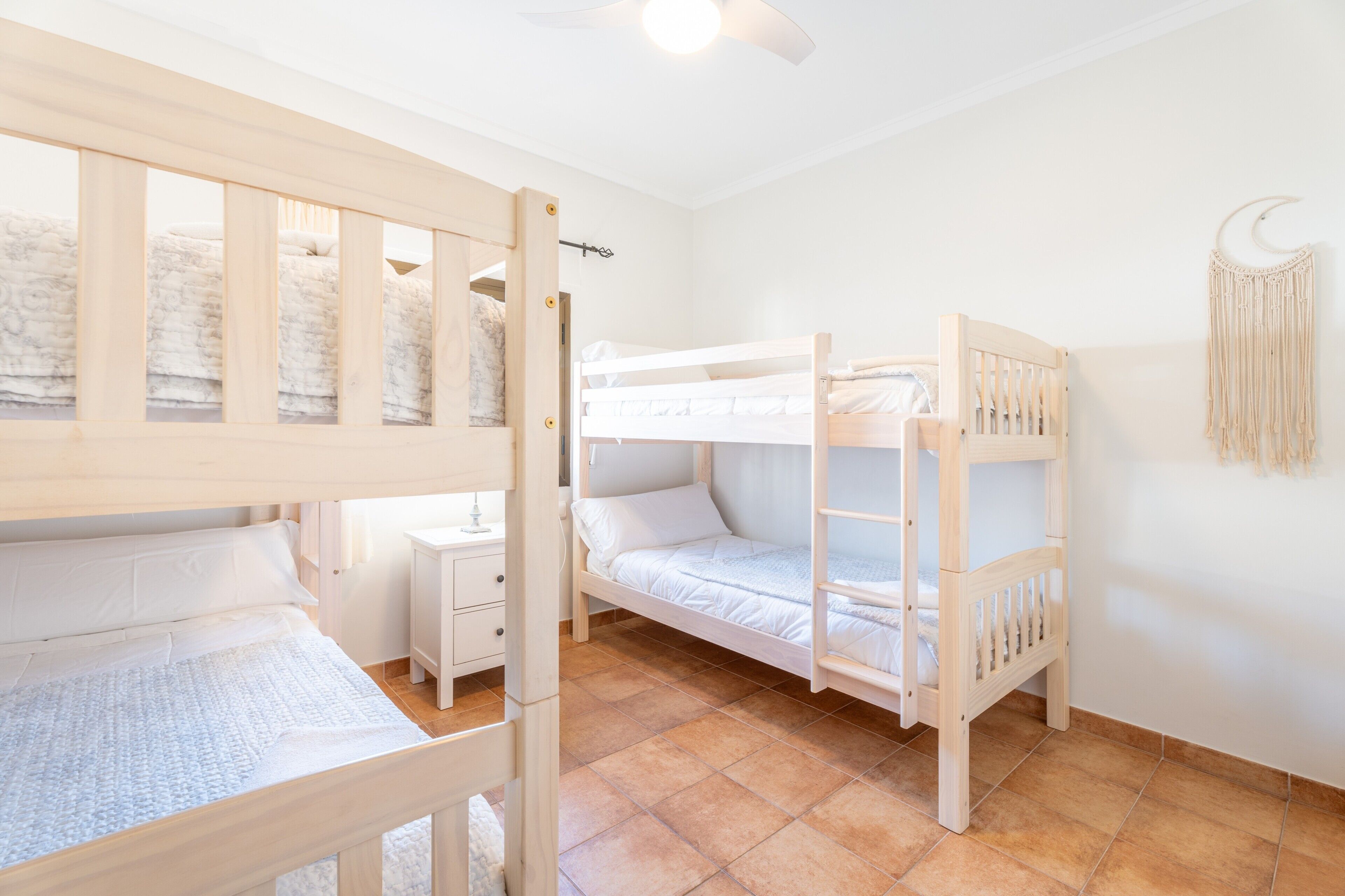 A room with bunk beds, a desk, and a wall-mounted macrame decoration.
