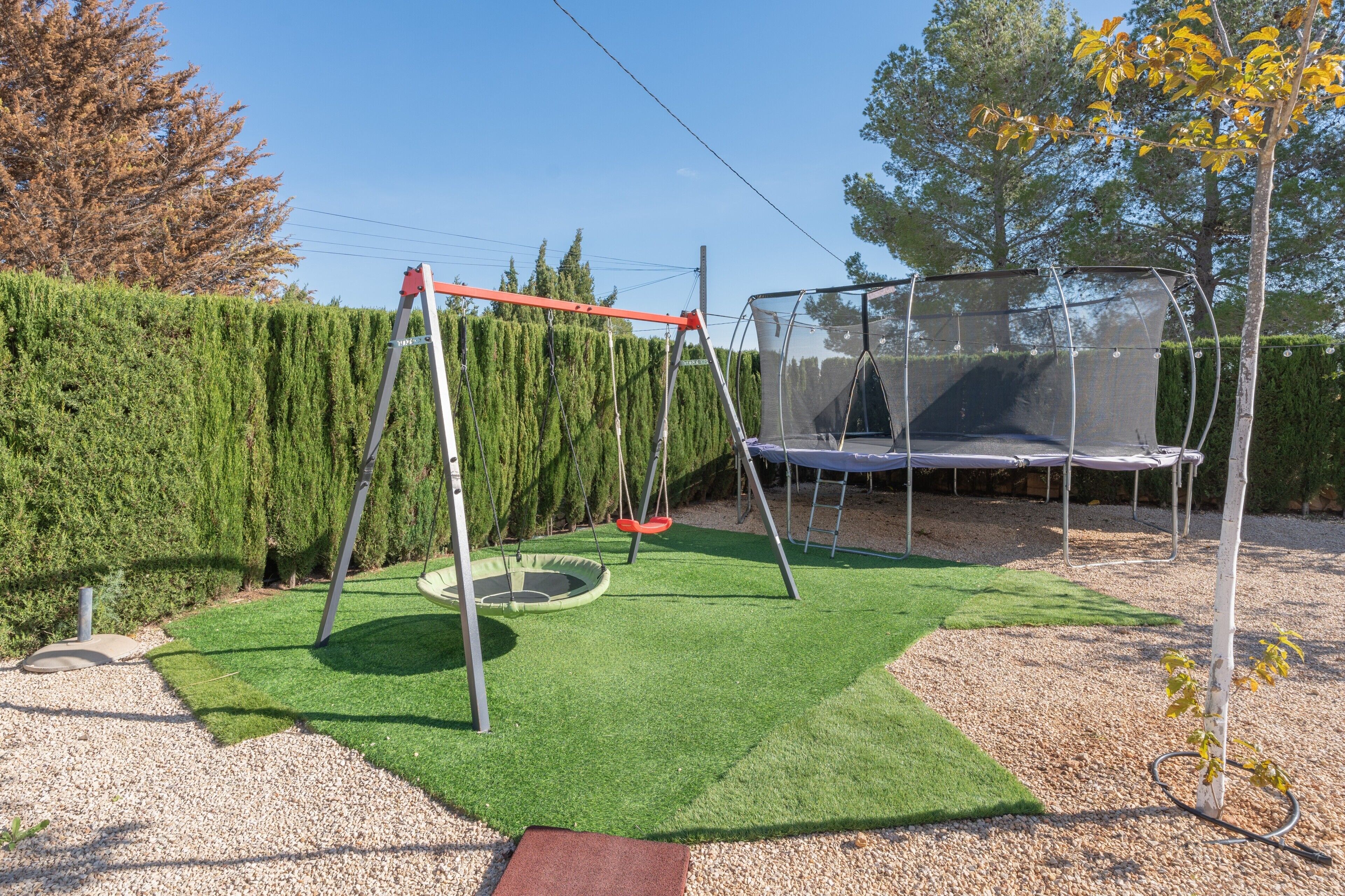 Un trampolín, un conjunto de columpios y césped artificial en un área de juegos al aire libre.