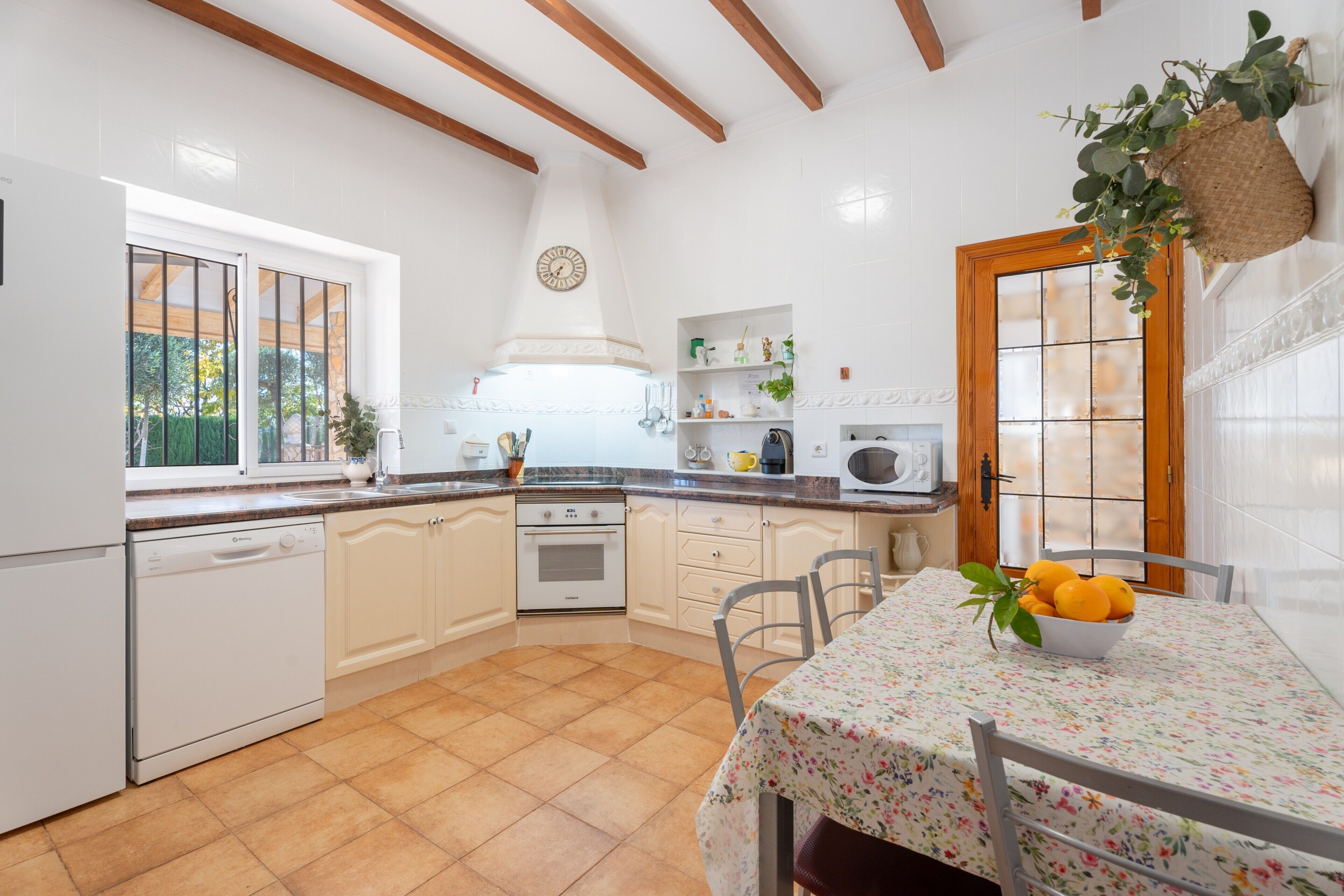 Une cuisine avec des meubles blancs, un lave-vaisselle, une cuisinière et un évier. Il y a une fenêtre qui donne sur un paysage verdoyant.