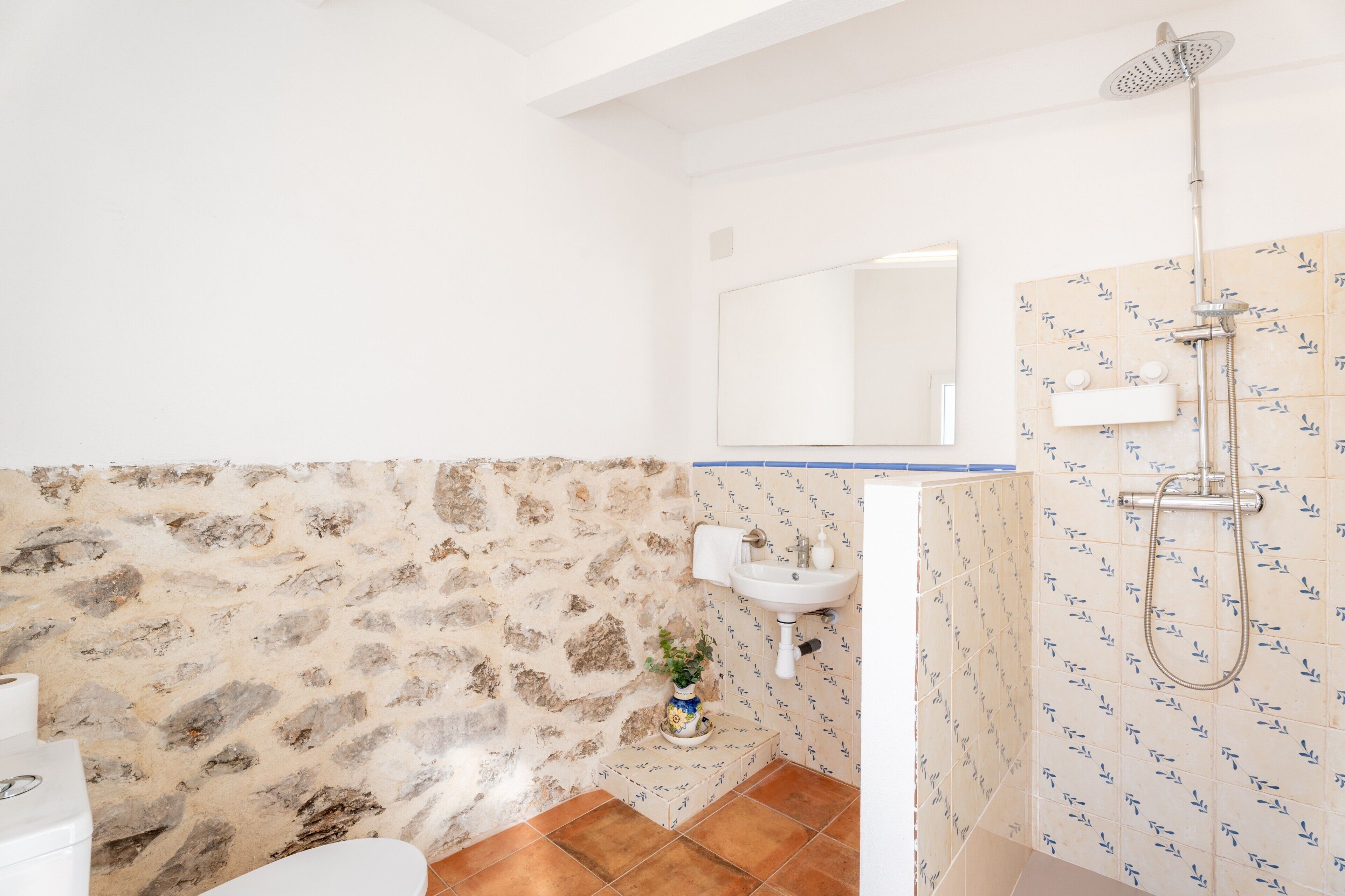 Un baño con pared de piedra, lavamanos, espejo y ducha.