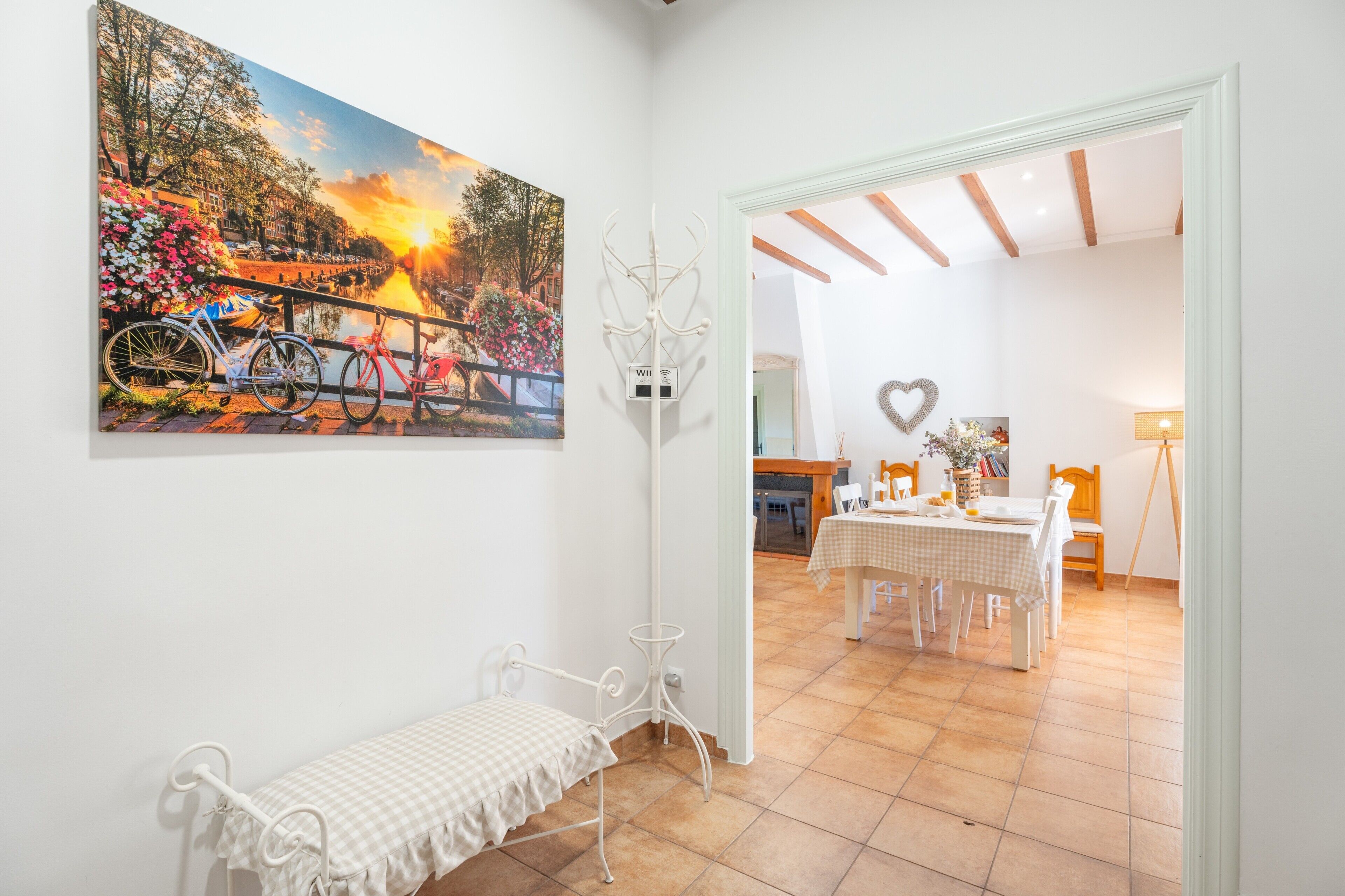 Una habitación con un banco, una mesa de comedor y un cuadro de un paisaje.