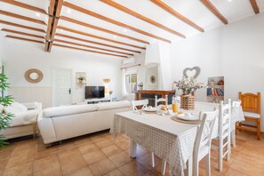 A modern living room with a sofa, dining table, and chairs, wooden beams on the ceiling, and a TV. - Holiday Home 'Reme ' with Private Pool, Wi-Fi and Air Conditioning (Navarres)