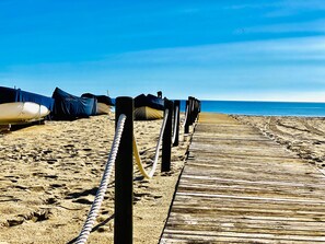 Ein hölzerner Steg führt zu Booten am Strand, einem Sandstrand und dem Meer.