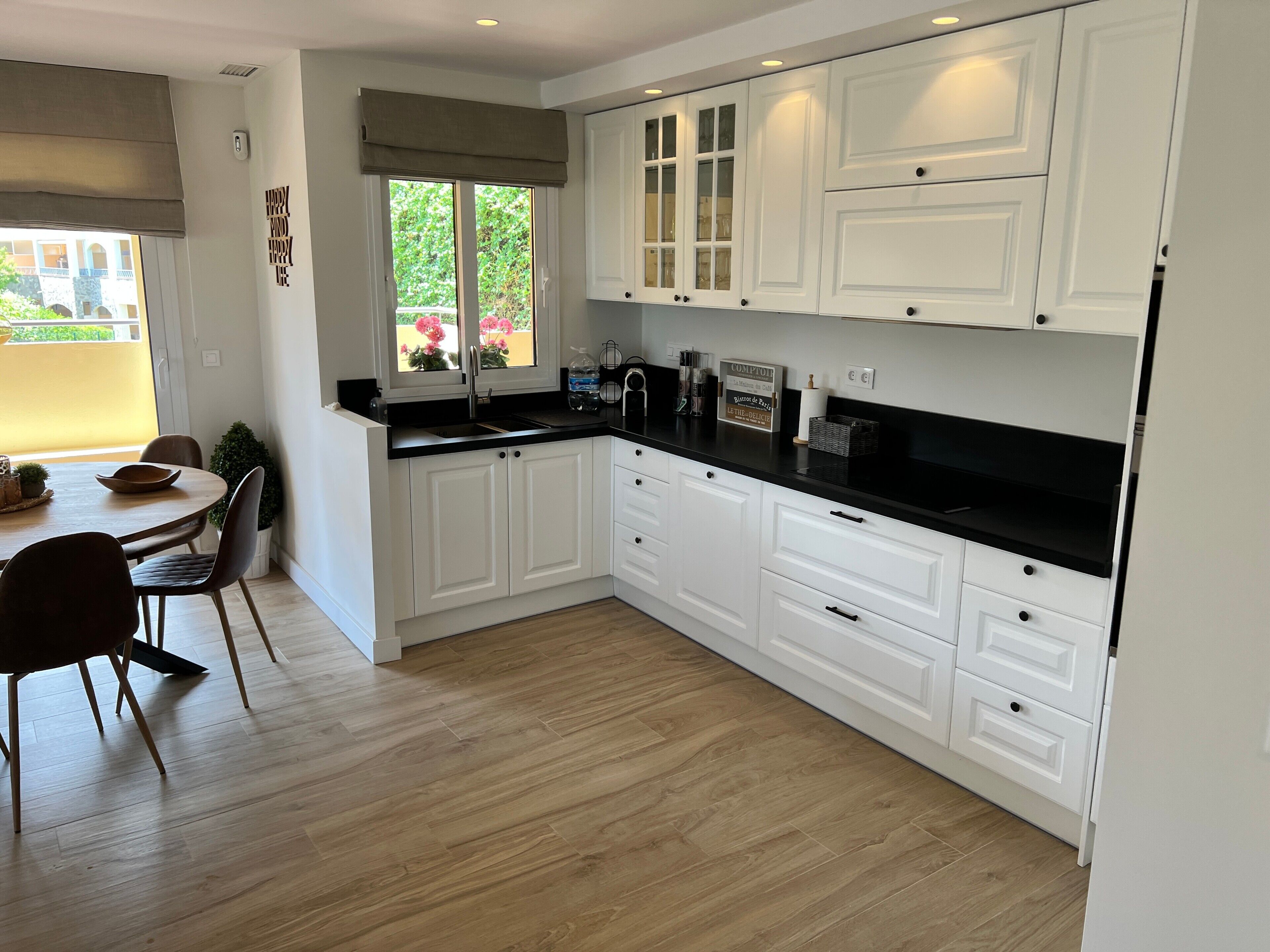 A modern kitchen with white cabinetry, a black countertop, and a dining area with a table and chairs.