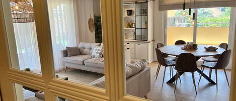 Un salon moderne avec un canapé, une table à manger, des chaises et une vue sur la verdure à l’extérieur.