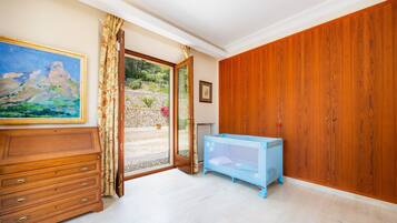 A room with a wooden dresser, a blue crib, a painting, and a view through a glass door.