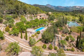 Uma villa em estilo mediterrâneo com piscina, rodeada por jardins bem cuidados e montanhas.