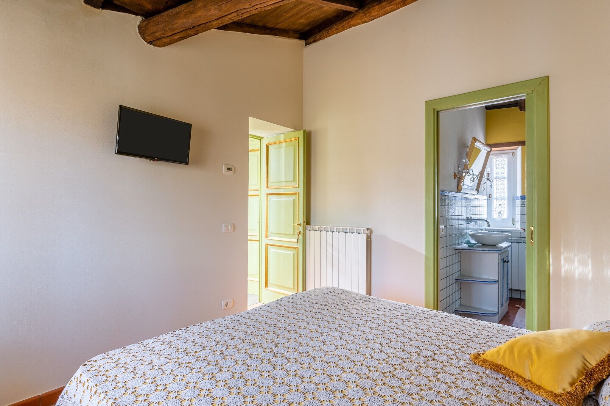 A bedroom with a bed, a television mounted on the wall, a door leading to a bathroom, and a radiator.