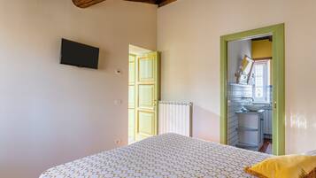 A bedroom with a bed, a television mounted on the wall, a door leading to a bathroom, and a radiator.