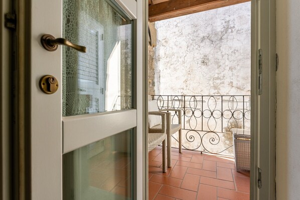 An open door to a balcony with a wrought iron railing, a wicker chair, and a wicker basket.