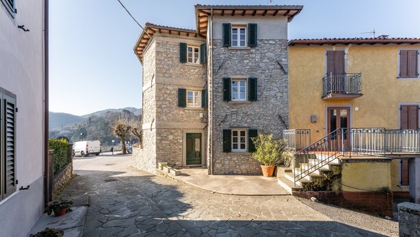 Un edificio de piedra con puerta verde, un balcón y una planta en maceta.
