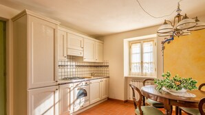 Una cocina con armarios blancos, salpicadero de azulejos, estufa y una mesa de comedor con sillas.