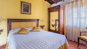 Un dormitorio con cabecera de madera, cama con colcha estampada, un espejo grande y una silla.