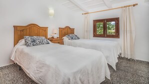 A room with two beds, a nightstand, a lamp, a window with curtains, and a ceiling with wooden beams. - Holiday Home 'Sontuiri Den Jaume' with Private Pool, Wi-Fi and Air Conditioning (Pollença)
