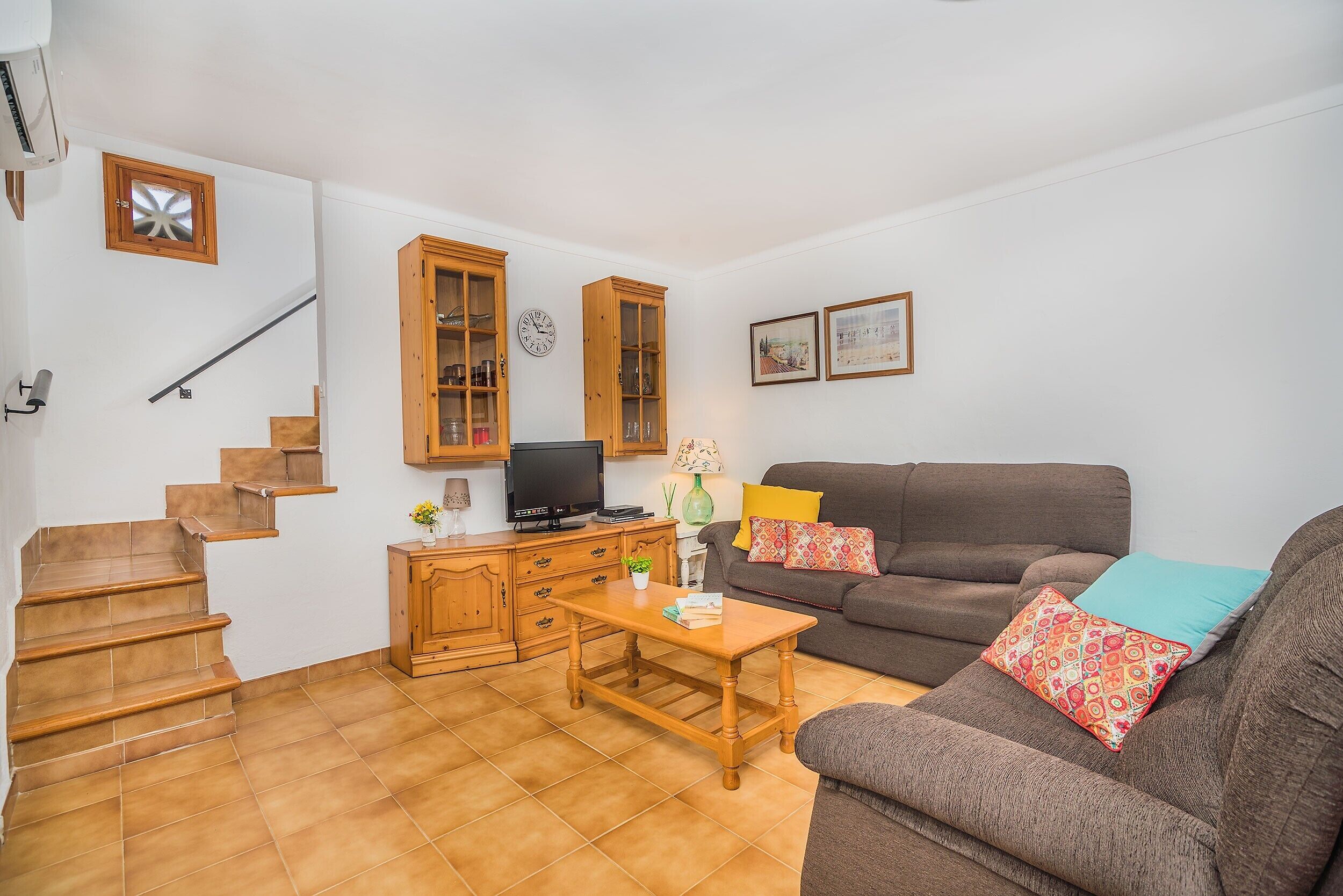 Un salon comprenant un canapé, une table basse, un téléviseur, des meubles en bois, un escalier et une horloge murale.