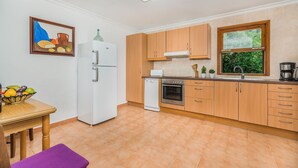 A kitchen with wooden cabinets, a white refrigerator, a dishwasher, and a window with a view of greenery. - Holiday Home 'Sontuiri Den Jaume' with Private Pool, Wi-Fi and Air Conditioning (Pollença)
