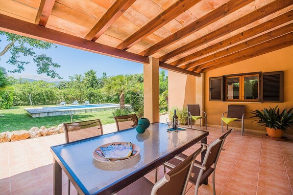 Une terrasse extérieure avec une table, des chaises et une vue sur une piscine et un espace verdoyant.