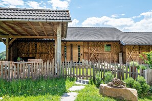 Un bâtiment rustique en bois, doté d’un toit en tuiles, d’une clôture en bois et d’un chemin de pierre menant à un banc en bois.