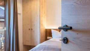 A bedroom with a wooden bed frame, a bedside table, and a window with curtains. - Apartment "Aschnerhof Holzhitt" with Mountain View, Private Balcony & Wi-Fi (Renon)