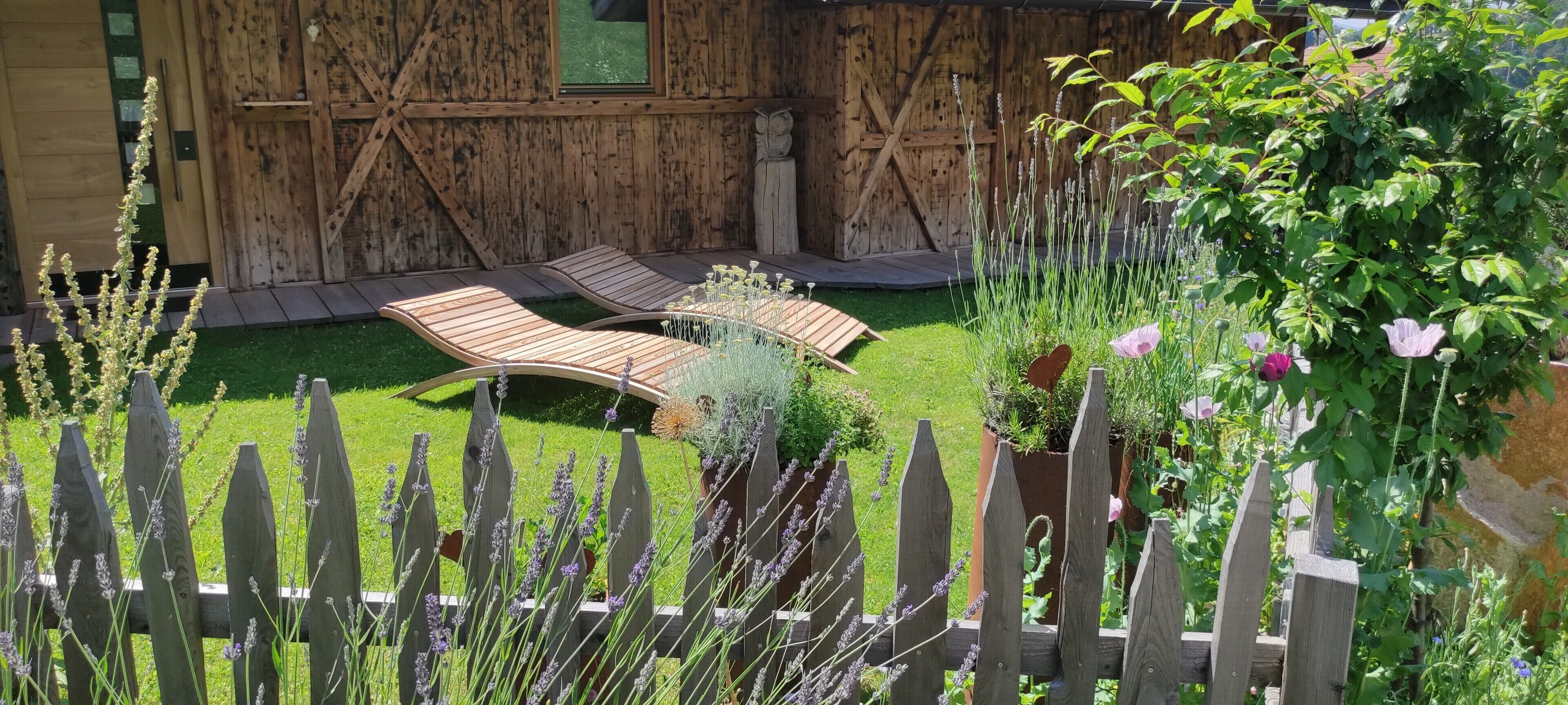 A wooden deck with lounge chairs, a wooden fence, and a garden with various plants and flowers.