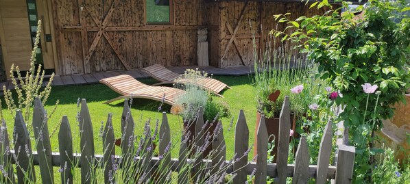 Une terrasse en bois avec des chaises longues, une clôture en bois et un jardin agrémenté de diverses plantes et fleurs.